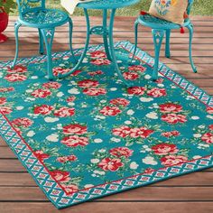 an outdoor area rug with flowers on it and two blue chairs in front of the table