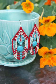 red, white and blue beaded earrings sitting on a saucer next to flowers