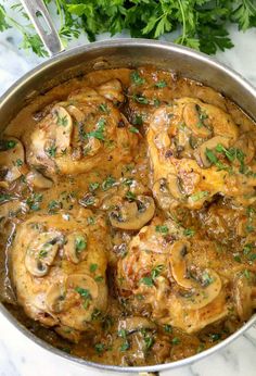 chicken with mushrooms and parsley in a pan on a marble countertop next to fresh parsley