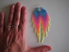 a pair of colorful beaded earrings sitting on top of a table next to a person's hand