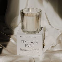 a glass candle sitting on top of a box next to a white sheet covered bed