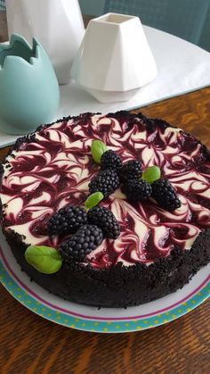 a chocolate cake with berries and cream on top sits on a plate next to a vase