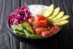 a bowl filled with sushi and vegetables on top of a wooden table next to rice