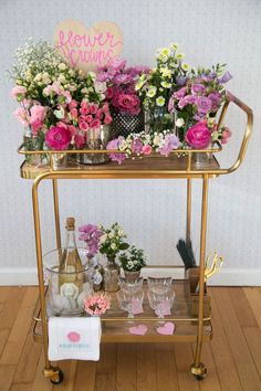 a gold bar cart with flowers and wine glasses on the bottom shelf, next to a sign that says flower power