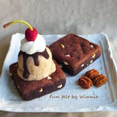 two pieces of brownies with ice cream and nuts on a white square plate next to each other