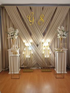 two gold and white vases with flowers in front of a wall decorated with drapes