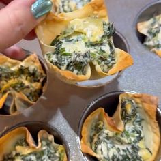 spinach and cheese appetizers in metal pans being held by someone's finger