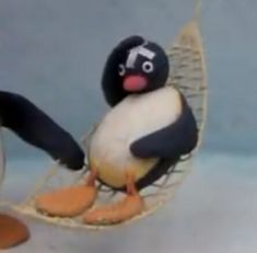 a toy penguin sitting in a hammock with an egg on it's back