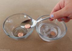 a person is spooning coins into two glass bowls with water and sand in them