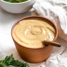 a bowl of dip with a wooden spoon in it next to a white napkin and green leafy vegetables