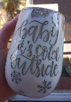 someone is holding up a wine glass decorated with snowflakes and glitters that says baby it's cold outside