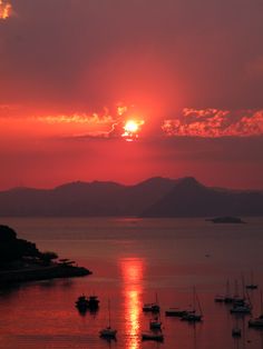 the sun is setting over water with boats in it and mountains in the distance,