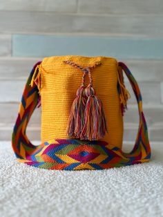 a small yellow bag with tassels on the front and side, sitting on a white carpet