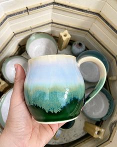 a hand holding a green and blue coffee cup