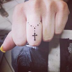 a person with a small cross tattoo on their thumb and finger, holding onto a bar