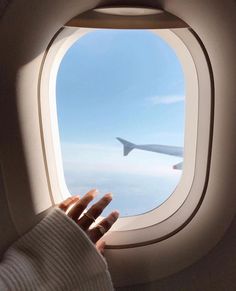 someone is holding their hand out the window of an airplane as it flies in the sky