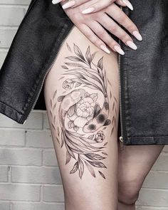 a woman's thigh with flowers and leaves tattoo on her leg, next to a brick wall