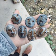 a person is holding five stone carvings in their hand, with faces painted on them