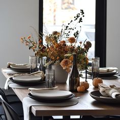 a dining table with plates and vases filled with flowers on top of the table