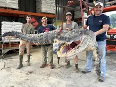 three men standing next to an alligator in a warehouse