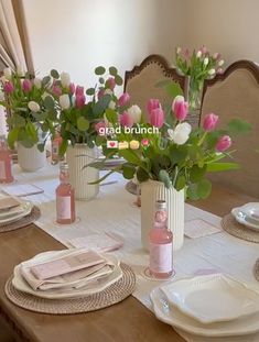 the table is set with pink and white tulips in vases on it