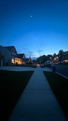 a long sidewalk in front of some houses at night with the moon rising over them