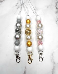 three different colored beads with caramel, white, and silver charms on a marble surface