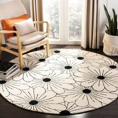 a white rug with black flowers on it in front of a chair and potted plant