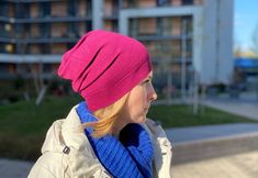 a woman wearing a pink hat and blue scarf standing in front of a tall building