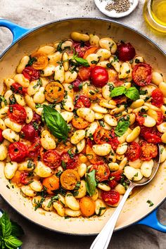 a pan filled with pasta, tomatoes and spinach on top of a blue table cloth