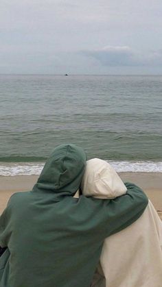 two people sitting on the beach looking out at the ocean and one person is wrapped in a blanket