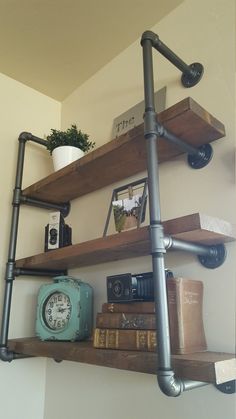 a shelf with some books and a clock on it next to a wall mounted pipe