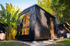 a small black house sitting on top of a lush green field next to a tree