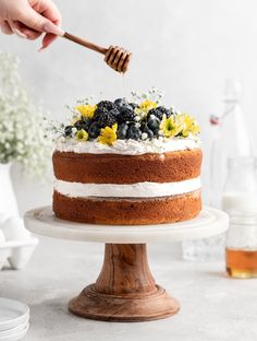 a person is decorating a cake with flowers and honey on the top while holding a wooden spatula