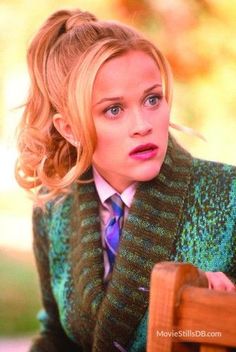 a woman with blonde hair wearing a green sweater and purple tie sitting on a wooden chair