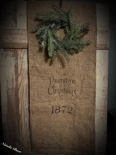 a christmas wreath hanging from the side of a wooden wall with primitive sayings on it