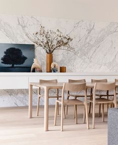 a dining room with marble walls and wooden chairs in front of a large painting on the wall