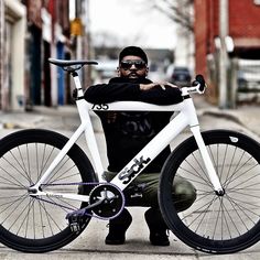 a man sitting on the ground next to a white bike with black spokes and seat