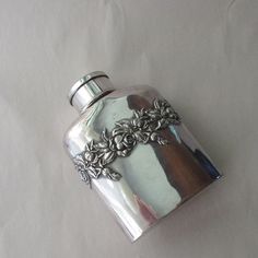 a silver flask shaped like a cross with leaves on the top and an embellishment in the middle