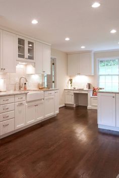 a large kitchen with white cabinets and wood floors is pictured in this image, there are lights on above the sink