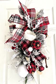 a red and white christmas wreath with pine cones, snowflakes and plaid ribbon