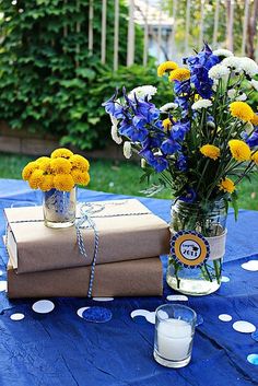 two vases filled with yellow and blue flowers sitting on top of a blue table cloth