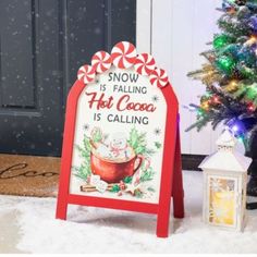 a snow is falling hot cocoa sign next to a christmas tree