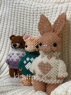 three small stuffed animals sitting on top of a white couch covered in beadwork