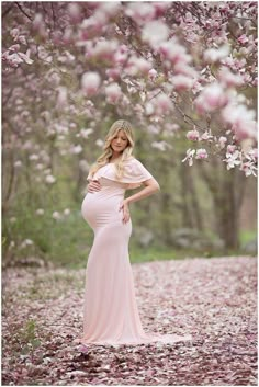 a pregnant woman in a pink dress standing under a tree with flowers on it's branches