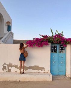 a woman leaning against a wall with flowers growing on it and a blue door in the background