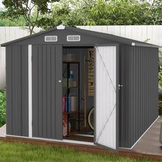 a small shed with the door open on a deck in front of some trees and grass