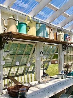 an old window is filled with pots and pans on a wooden table in front of a greenhouse