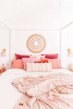 a bed with pink and orange pillows on top of it next to a white wall