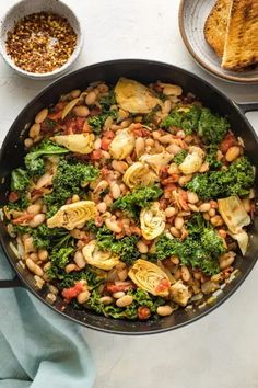 a skillet filled with beans, broccoli and other vegetables next to bread